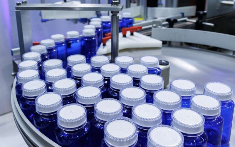 blue plastic bottle on production line of conveyor belt at filling machine in medical factory
